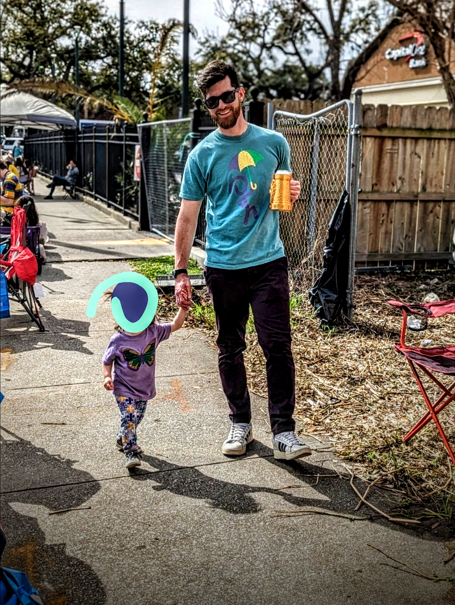 Bearded man walking with child down a street during Mardi Gras while wearing Jaunty Secondline Leader t-shirt.