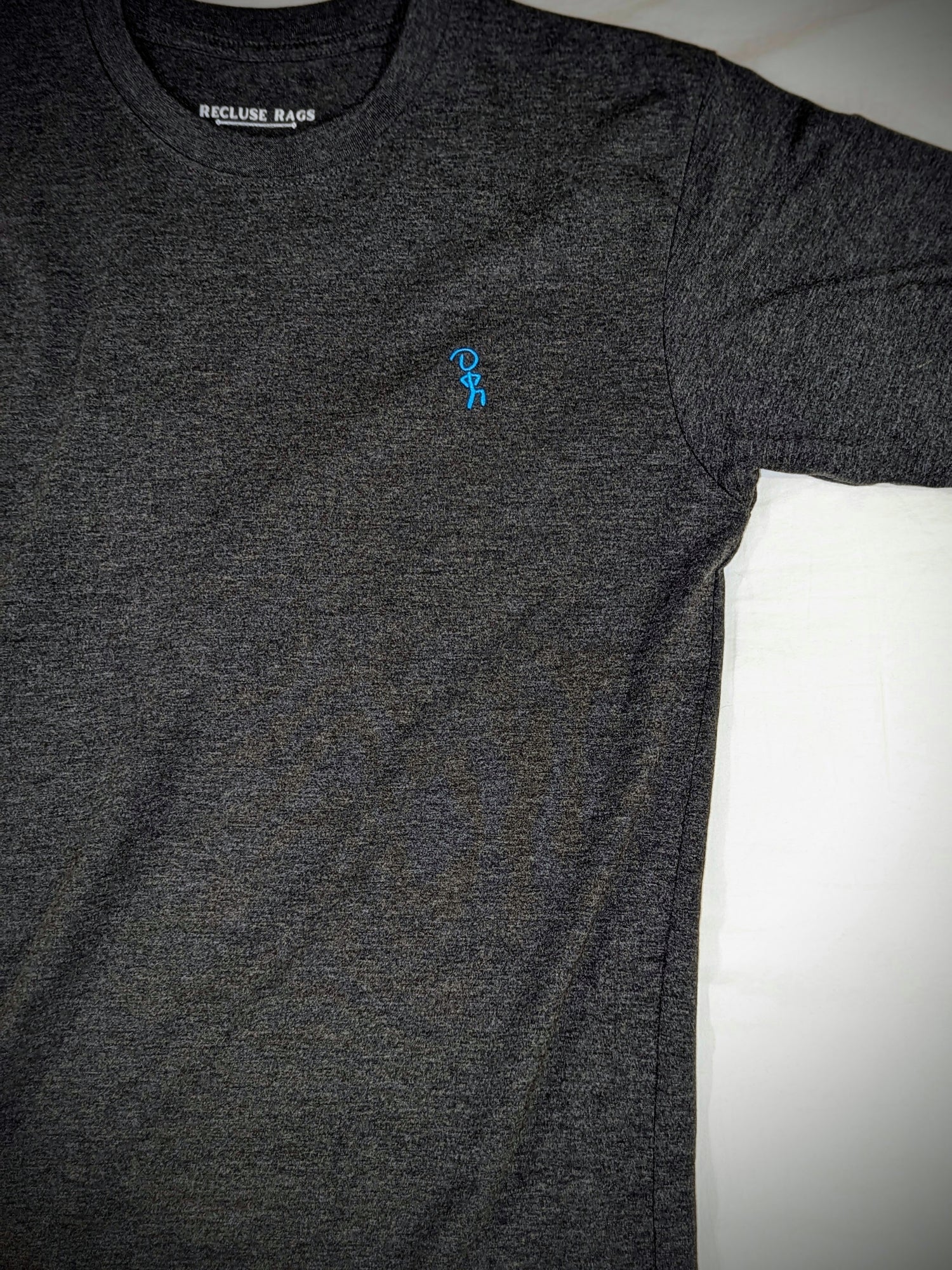Highly contrast image of blue embroidered Jaunty Man on premium charcoal t-shirt.