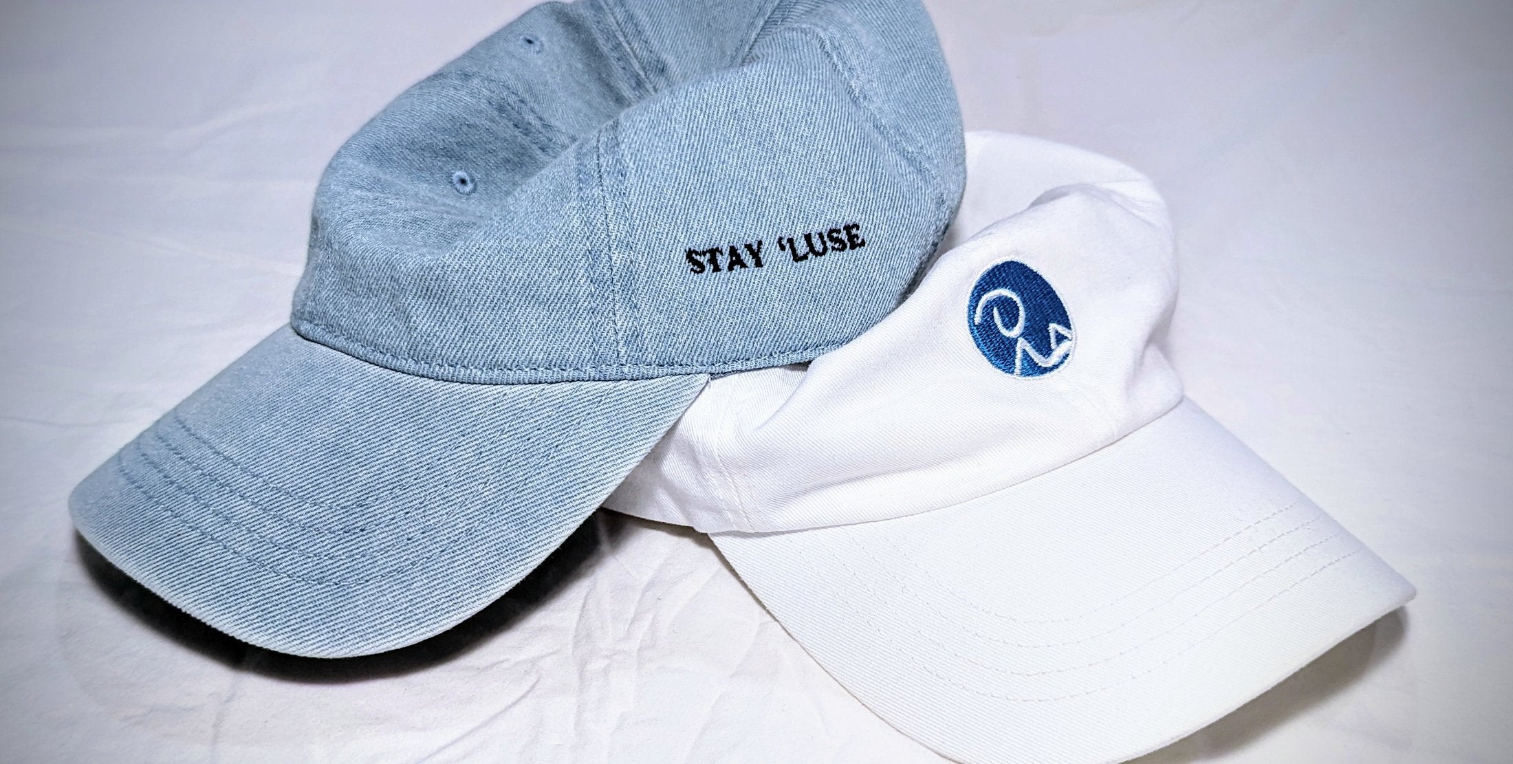 Light blue Stay 'luse denim hat (Stay 'luse is an abbreviation of Recluse) stacked on top of Recluse Rags Classic Dad hat.