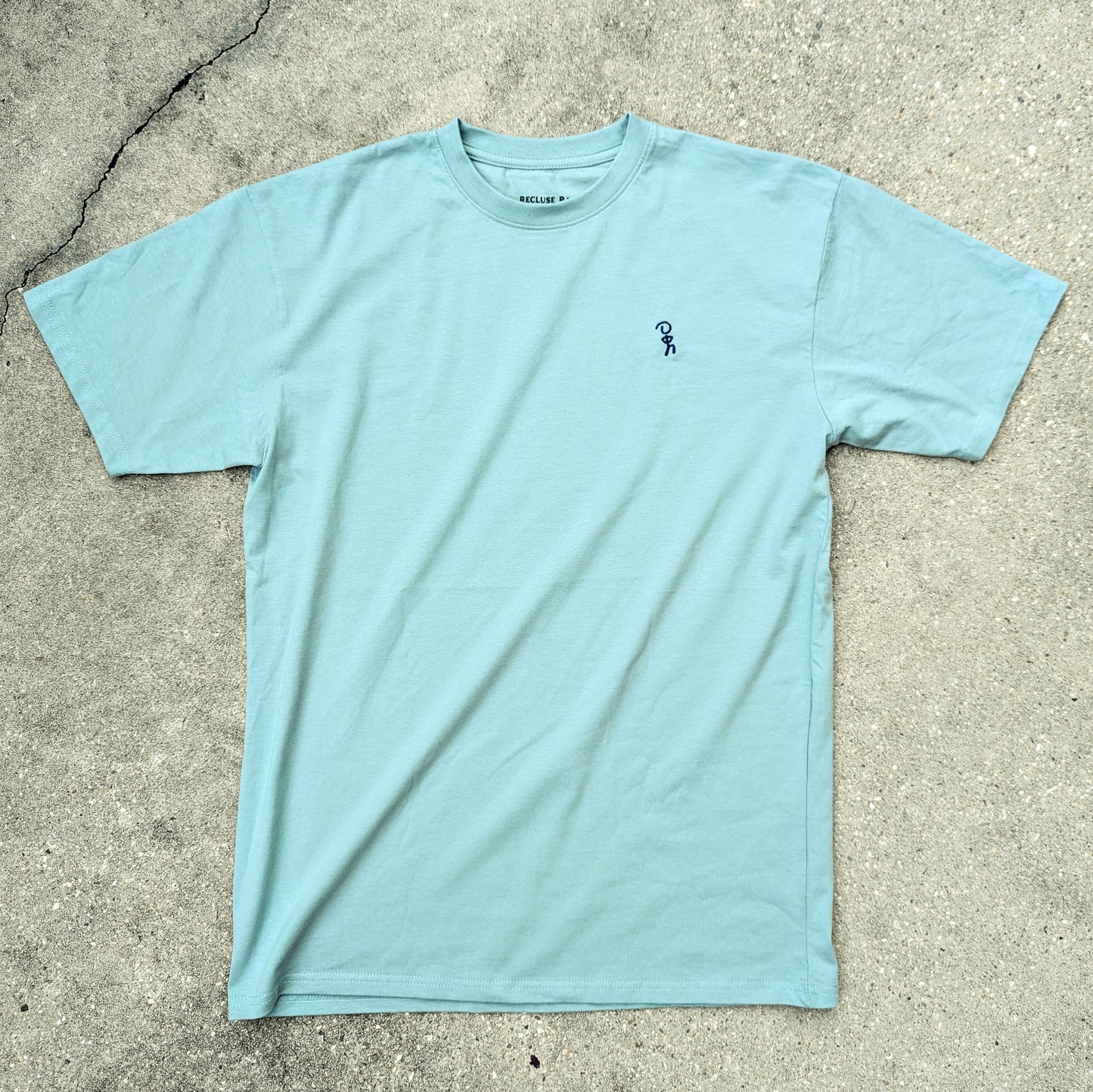 Men's agave blue short sleeve T-shirt laid flat. Navy Embroidered Jaunty Man design on left chest.