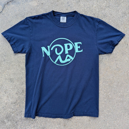Recluse Rags Nope logo in cyan on Navy t-shirt. Laid out on concrete.