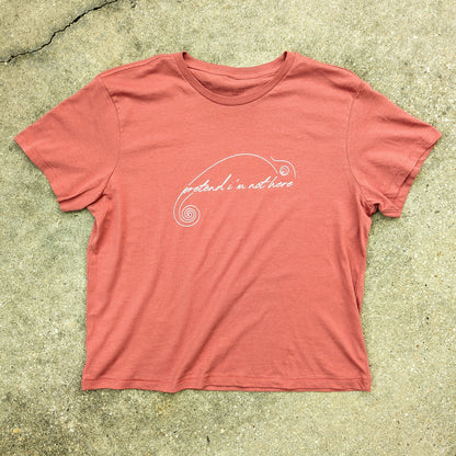 Women's Red T-shirt laid flat. "Pretend I'm not here" written in script in a minimalist chameleon design printed in white on the front center.