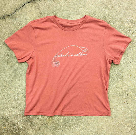 Women's Red T-shirt laid flat. "Pretend I'm not here" written in script in a minimalist chameleon design printed in white on the front center.