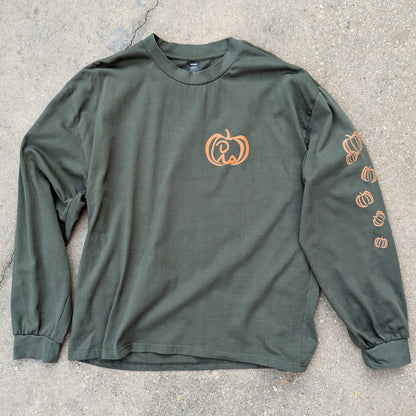 Oversized, long sleeve t-shirt in cypress color laid out on concrete, with Jaunty Man reclined inside pumpkin on left chest and varied pumpkins down left sleeve. all colored a rusty orange shade.