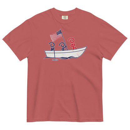 A red short sleeve t-shirt laid flat. Front graphic shows three Jaunty Men in a simple boat carrying an American flag, similar to George Washington crossing the Delaware.