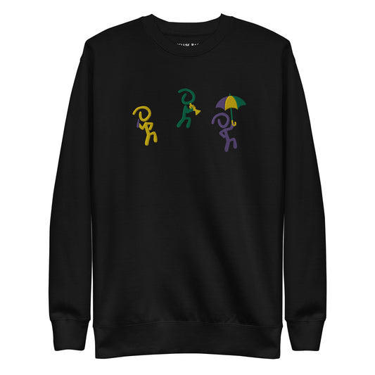 Black sweater with 3 "Jaunty Man" stick figures embroidered in gold, green, and purple, and holding a drink, a trumpet, and an umbrella, respectively.