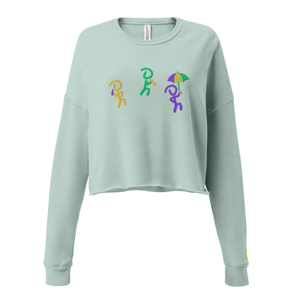 Dusty blue cropped sweater with 3 "Jaunty Man" stick figures embroidered in gold, green, and purple, and holding a drink, a trumpet, and an umbrella, respectively.